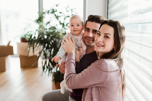 Ein Porträt eines glücklichen jungen Paares mit einem Baby und Kartons beim Umzug in ein neues Haus. - HPIF30739