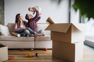 A portrait of happy young couple with a baby and cardboard boxes, moving in a new home. - HPIF30745