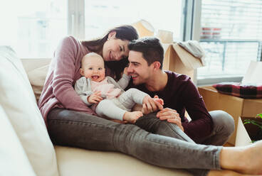Ein Porträt eines glücklichen jungen Paares mit einem Baby und Kartons beim Umzug in ein neues Haus. - HPIF30750