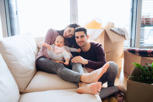 Ein Porträt eines glücklichen jungen Paares mit einem Baby und Kartons beim Umzug in ein neues Haus. - HPIF30751