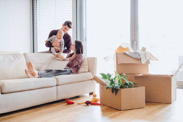 A portrait of happy young couple with a baby,laptop and cardboard boxes, moving in a new home. - HPIF30754