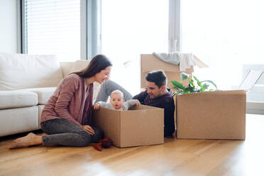 Ein Porträt eines glücklichen jungen Paares, das mit einem Baby und Kartons auf einem Sofa sitzt und in ein neues Haus zieht. - HPIF30756