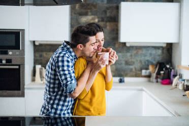 A young happy couple standing in a kitchen at home, drinking coffee. - HPIF30768