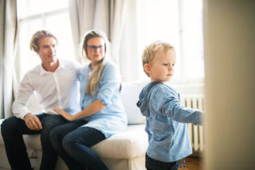 Happy young happy parents looking at their toddler son inside in a bedroom. - HPIF30784