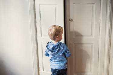 A rear view of toddler boy standing near wardrobe door inside in a bedroom. Copy space. - HPIF30785