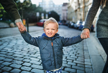 A small toddler boy with unrecognizable parents walking outdoors in city, holding hands. - HPIF30801