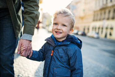 A small toddler boy with unrecognizable father walking outdoors in city, holding hands. - HPIF30810