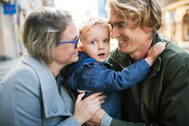 Young happy parents hugging their toddler son outdoors in city. - HPIF30813