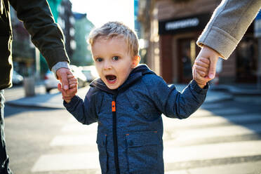 A small toddler boy with unrecognizable parents walking outdoors in city, holding hands. - HPIF30816