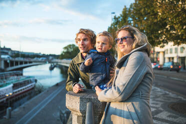 Young parents with their toddler son standing outdoors by the river in city of Prague. - HPIF30821