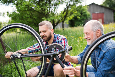 An adult hipster son and senior father repairing bicycle outside on a sunny summer day. - HPIF30902