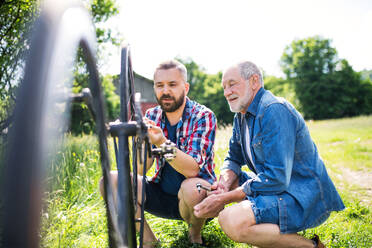 An adult hipster son and senior father repairing bicycle outside on a sunny summer day. - HPIF30904