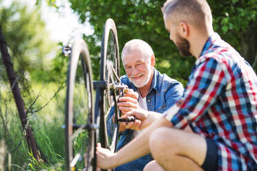 An adult hipster son and senior father repairing bicycle outside on a sunny summer day. - HPIF30906