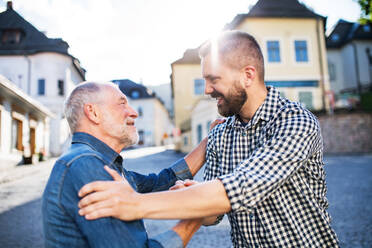 An adult hipster son with his senior father on a walk in town, greeting. - HPIF30922