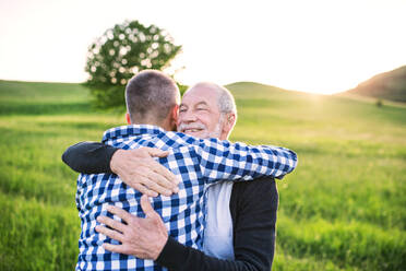 An adult hipster son with his senior father on a walk in nature at sunset, hugging. Copy space. - HPIF30938