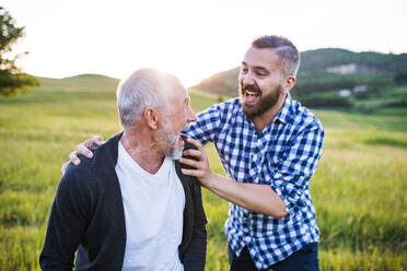 An adult hipster son with his senior father on a walk in nature at sunset, having fun. - HPIF30939