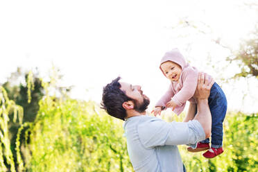 A handsome father holding his toddler daughter outside in green sunny spring nature. - HPIF30967