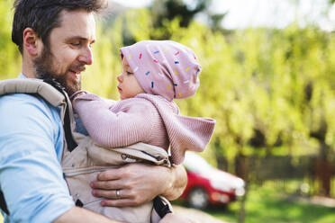 A father with his toddler daughter in a baby carrier outside on a spring walk. Copy space. - HPIF30970