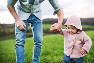 An unrecognizable father with his toddler daughter outside in green sunny spring nature. - HPIF30982