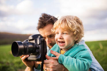 A father and his toddler son with a camera outside in green sunny spring nature. - HPIF30990