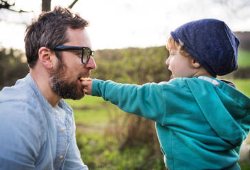 A cute toddler boy giving his father a biscuit outside in spring nature. - HPIF30992