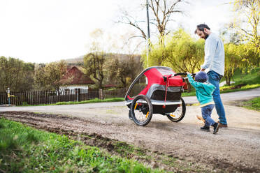 A father with toddler son pushing a jogging stroller outside. A walk in spring nature. - HPIF30993