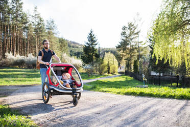 A father with two toddler children sitting in jogging stroller on a walk outside in spring nature. - HPIF30995