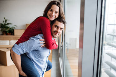 Young happy couple moving in a new home, having fun. A man giving a woman a piggyback ride. - HPIF31026