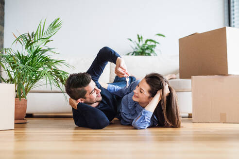 A young happy couple with a key and cardboard boxes lying on a floor, moving in a new home. - HPIF31030