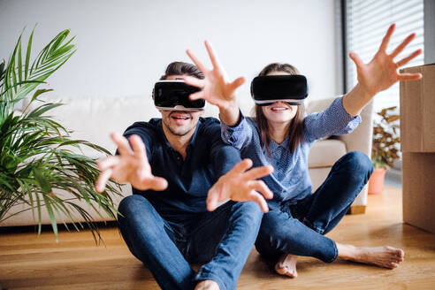 A young couple with VR goggles and cardboard boxes sitting on a floor, moving in a new home. - HPIF31031