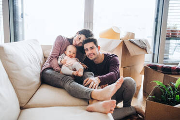 A portrait of happy young couple with a baby and cardboard boxes, moving in a new home. - HPIF31033