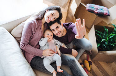 A portrait of happy young couple with a baby and cardboard boxes, moving in a new home. A top view. - HPIF31034