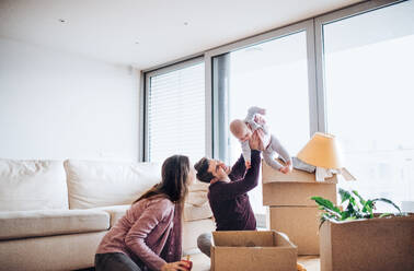 Young couple with a baby and cardboard boxes sitting on a floor, moving in a new home. - HPIF31035