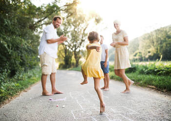 A young family with small children playing hopscotch on a road in countryside in summer. - HPIF31049