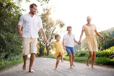 A young family with small children playing hopscotch on a road in countryside in summer. - HPIF31050