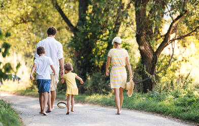 A rear view of young family with small children walking barefoot on a road in summer nature. - HPIF31054