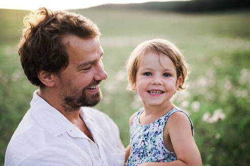 Handsome young father in green sunny summer nature holding his cute small daughter in the arms. - HPIF31098