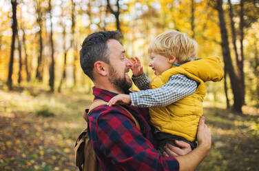 A mature father standing and holding a toddler son in an autumn forest, having fun. - HPIF31133