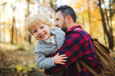 A mature father standing and holding a toddler son in an autumn forest, having fun. - HPIF31137