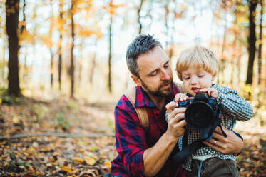 A mature father and a toddler son in an autumn forest, taking pictures with a digital camera. - HPIF31142