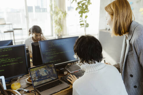 Manager discussing with programmer over computer at desk in office - MASF36952
