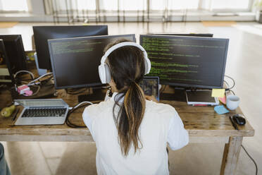 Rear view of male programmer working on computer at desk in creative office - MASF36959