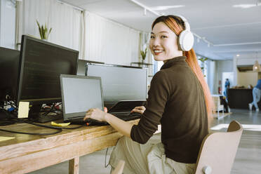 Portrait of smiling female programmer working on laptop in creative office - MASF36972