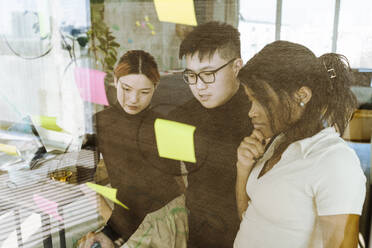 Multiracial male and female colleagues brainstorming over adhesive notes in creative office - MASF36974