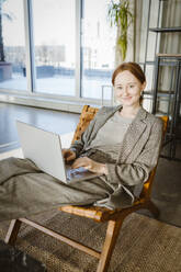 Portrait of smiling businesswoman using laptop while sitting in chair at office - MASF36989