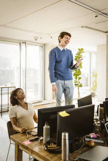 Happy entrepreneur standing on chair by colleague at desk in creative office - MASF36993