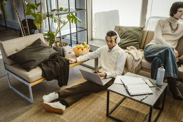 High angle view of programmer using mobile phone sitting with laptop on carpet in creative office - MASF37005