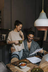 Smiling couple reading document while sitting at home - MASF37021