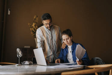 Boyfriend standing near non-binary person sorting bills on table at home - MASF37036