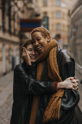 Happy non-binary couple embracing each other while standing at street - MASF37037